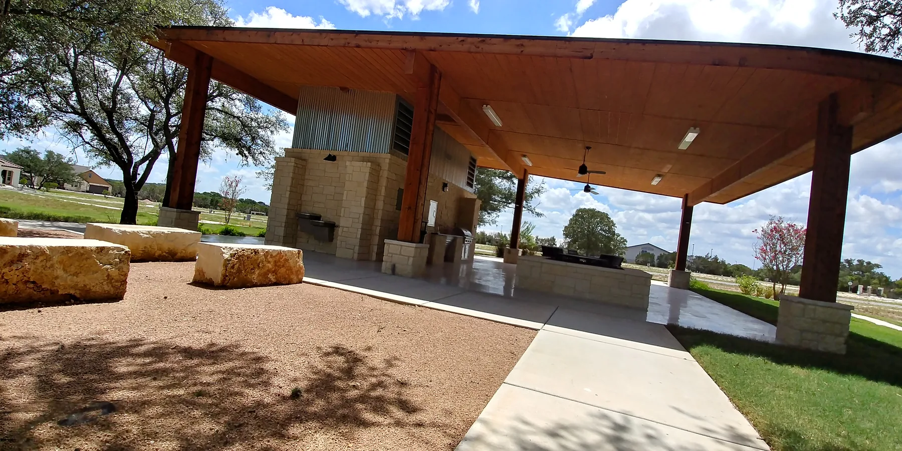 Open-sided wood-roof pavilion with a stone outdoor cooking area