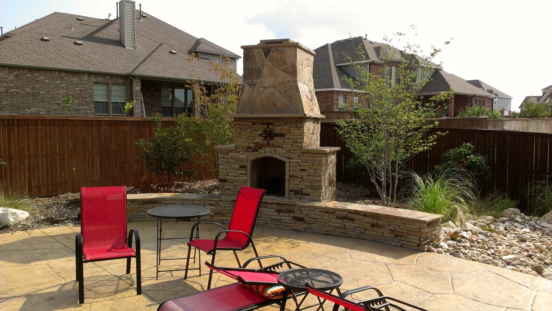 Stone outdoor fireplace and seating in a landscaped backyard